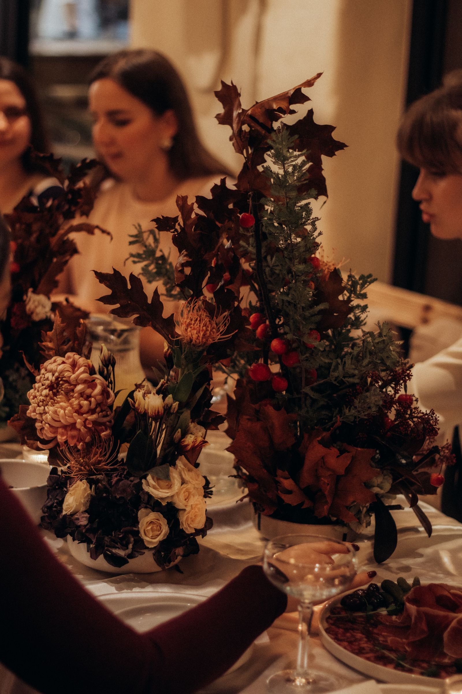 Cozy evening dinner with friends, featuring autumn floral arrangements and warm lighting.