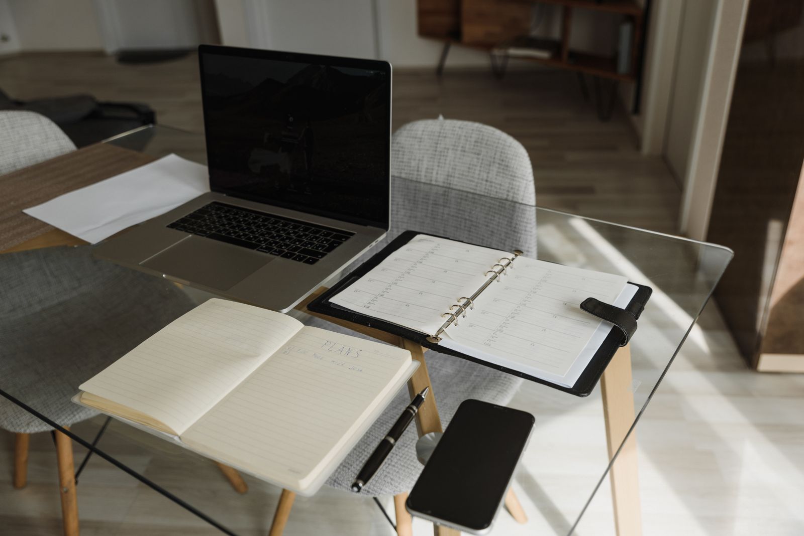 A clean and organized office setup with a laptop, notebook, and planner on a glass desk.