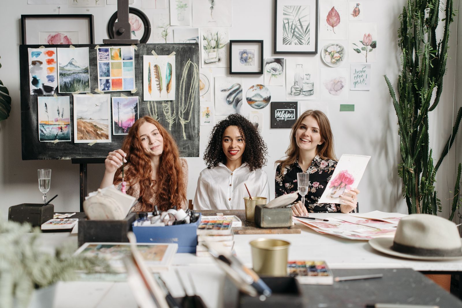 Three women enjoying an art workshop surrounded by paintings and art supplies.